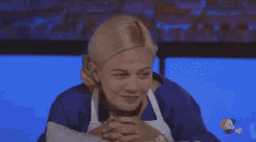 a woman wearing an apron is sitting at a table with her hands folded