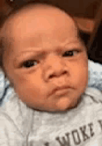 a baby is making a funny face and wearing a gray shirt with the word woke on it .