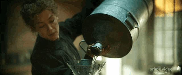 a woman pouring water from a large metal bucket
