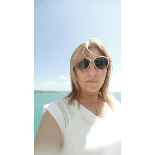 a woman wearing sunglasses and a white shirt is standing in front of a body of water