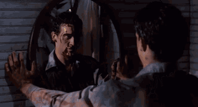 a man is looking at his reflection in a mirror with blood on his face .