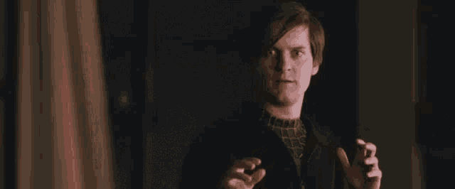 a man in a black jacket is standing in the dark with his hands outstretched .
