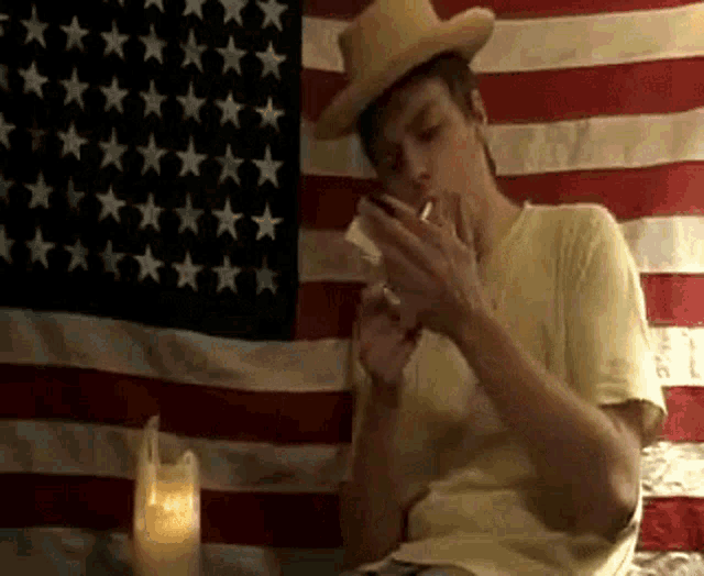 a man wearing a cowboy hat is smoking a cigarette in front of an american flag