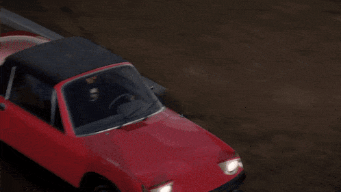 a red car with a black roof is driving down the road