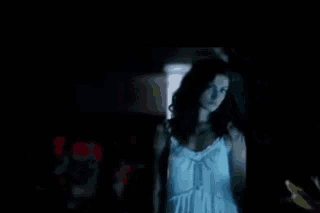 a woman in a white dress is standing in the dark in front of a door .