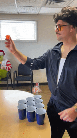 a man wearing sunglasses is playing beer pong