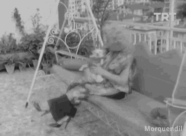 a black and white photo of a woman sitting on a swing with a dog .