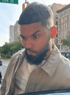a man with a beard is standing in front of a green sign that says 104 st