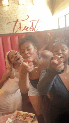 three women are posing for a picture in front of a sign that says trust