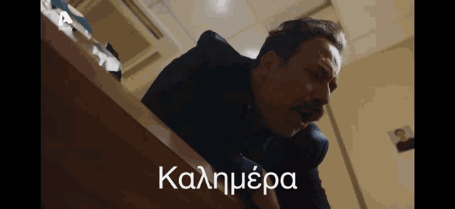 a man crawling over a desk with the words καλημερα written in a foreign language