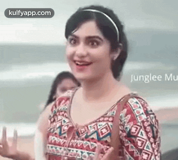 a woman is smiling and waving at the camera while standing on the beach .