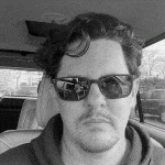 a man wearing sunglasses and a hoodie is sitting in a car .