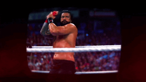 a shirtless wrestler is standing in a ring with his fist in the air .