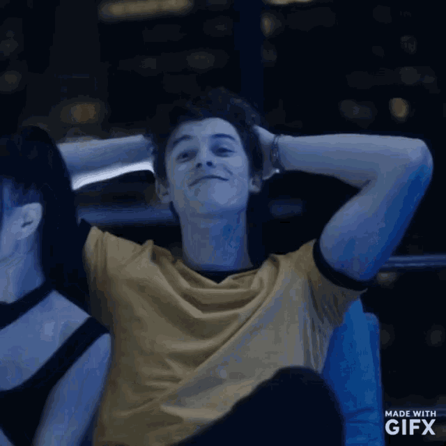 a man in a yellow shirt is sitting next to a woman with her hands behind her head .