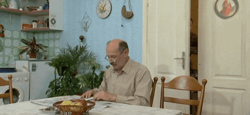 an older man sits at a table reading a magazine