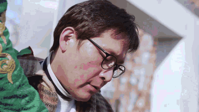 a man wearing glasses and a green jacket looks down at something