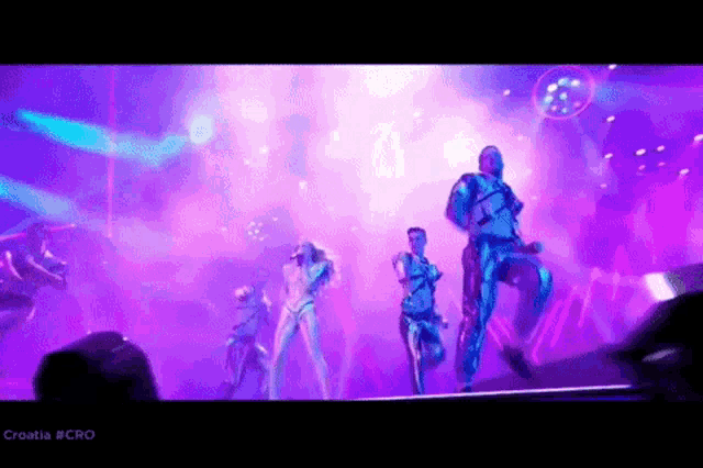 a group of people dancing on a stage with purple lights behind them