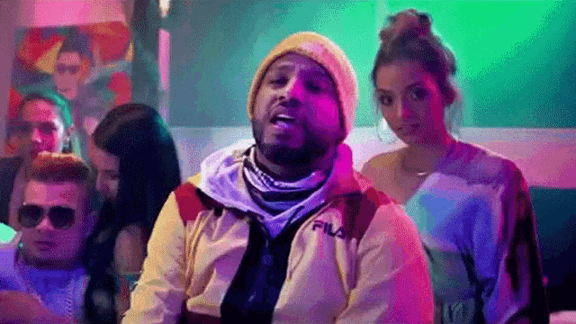 a man wearing a beanie and a jacket is standing in front of a group of people .