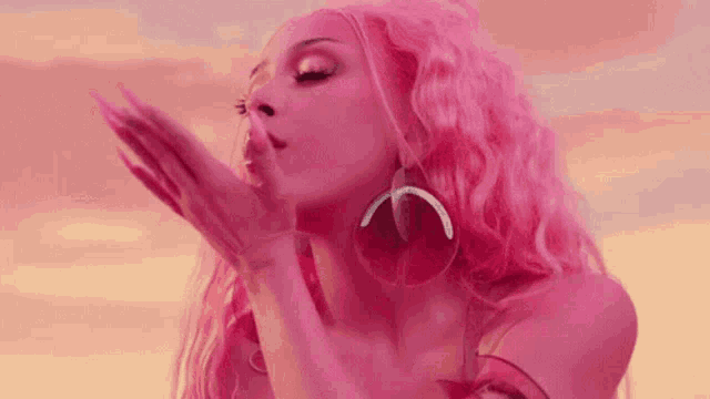 a close up of a woman with pink hair blowing a kiss .
