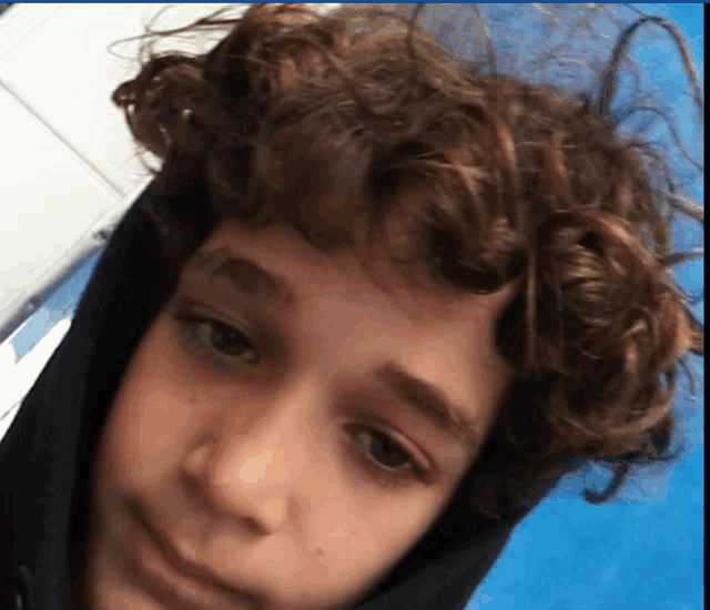 a young boy with curly hair is wearing a black hooded jacket