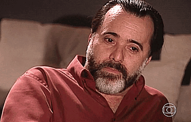 a man with a beard is wearing a red shirt with the letter o on the bottom right