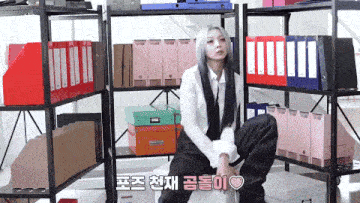 a woman is sitting in front of a shelf full of binders and boxes