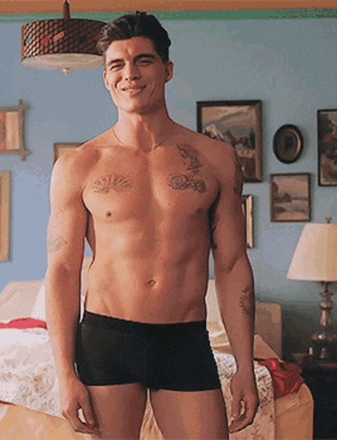 a shirtless man in black underwear is standing in a bedroom