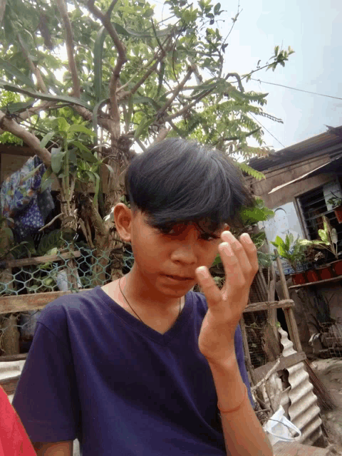 a young boy in a blue shirt holds his hand up to his forehead