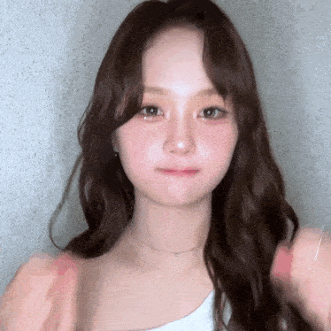 a close up of a woman 's face with long brown hair and a white top .