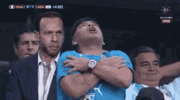 a man is sitting in a stadium with his hands on his chest and looking up .