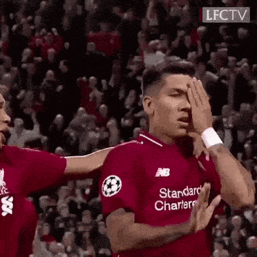 a soccer player in a red jersey is covering his face with his hands while another player hugs him .