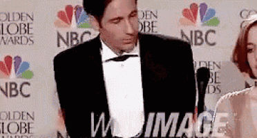a man in a tuxedo is standing in front of a microphone at a nbc golden globe awards .