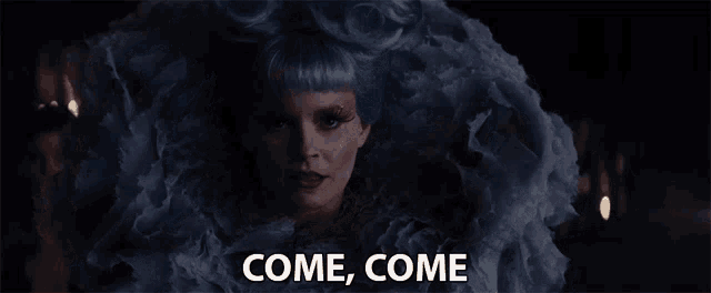 a woman with blue hair is wearing a ruffled dress and says come come