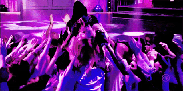 a crowd of people are gathered in a purple room with a tntp logo