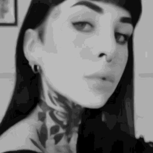 a black and white photo of a woman with a tattoo on her neck and nose .
