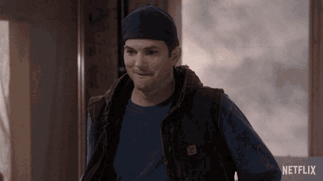 a man wearing a vest and a beanie is standing in front of a sign that says netflix