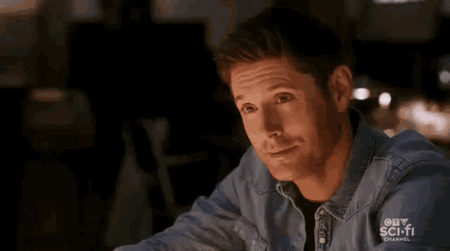 a man in a denim jacket is sitting at a table and smiling .