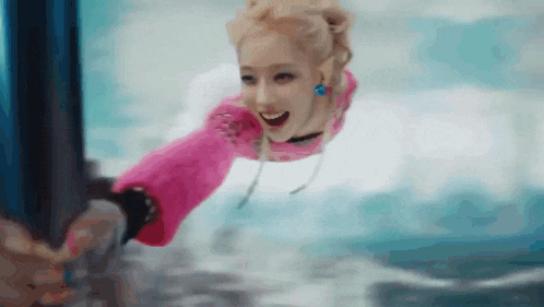 a woman in a pink sweater is flying through the air over the ocean .