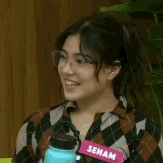 a woman wearing glasses and a plaid shirt is smiling in front of a sign that says virtual gifts update as of