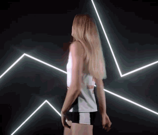 a woman in a white tank top and black shorts is standing in front of a wall of neon lights