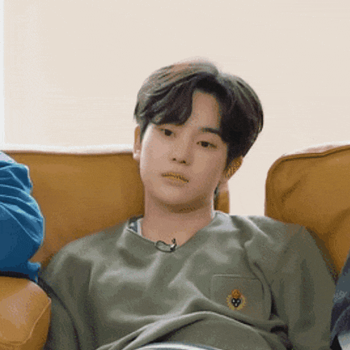 a young man sitting on a couch wearing a green shirt