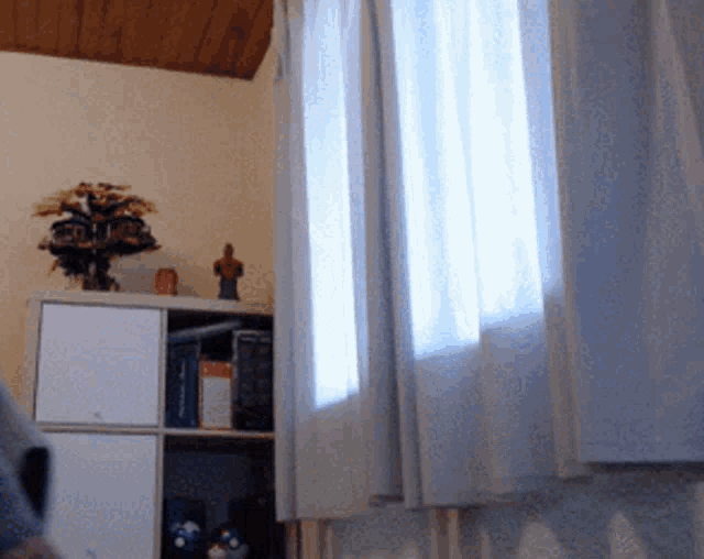 a room with white curtains and a shelf with a statue on top