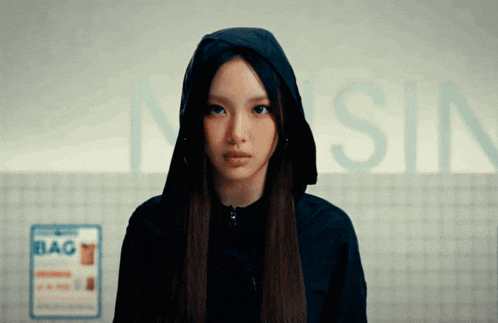 a woman wearing a hooded jacket stands in front of a sign that says " bag "