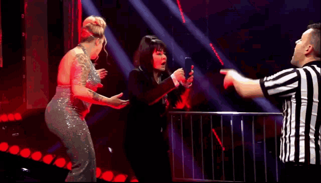two women are standing next to each other on a stage while a referee stands between them .