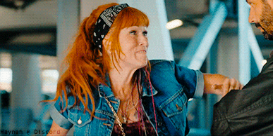 a woman with red hair wearing a bandana and a denim jacket holds a man 's hand