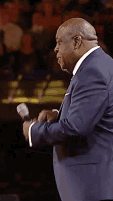 a man in a blue suit is holding a microphone in his right hand