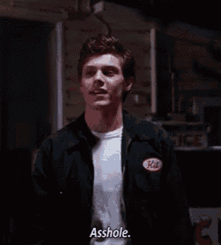 a man in a black jacket is standing in a dark room and says asshole