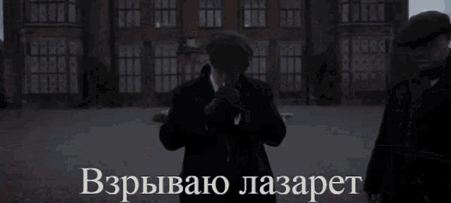a man in a suit stands in front of a large brick building with a caption in a foreign language
