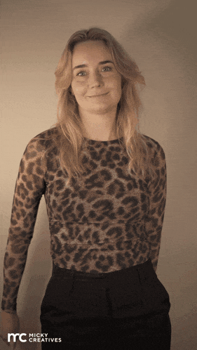 a woman wearing a leopard print shirt is standing in front of a micky creatives sign