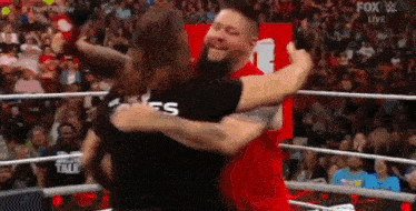 a man in a red shirt is hugging another man in a black shirt in a wrestling ring .